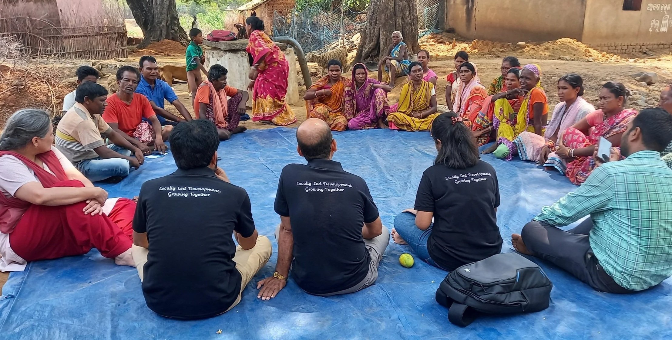Group seated in a circle on a blue tarp at a listening session in India
